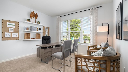 Modern home office featuring a desk, shelving with decor, stylish chairs, and natural light from large windows.
