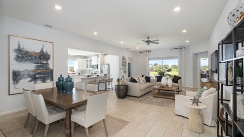 Bright, modern living room and dining area featuring stylish furniture, artwork, and large windows overlooking a green landscape.