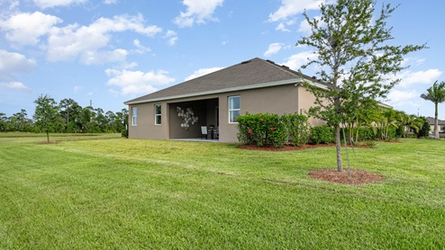 Exterior view of a modern house with a porch, surrounded by green grass and trees.