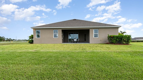 Rear view of a modern home with a spacious lawn and patio, featuring a small seating area under the covered porch.
