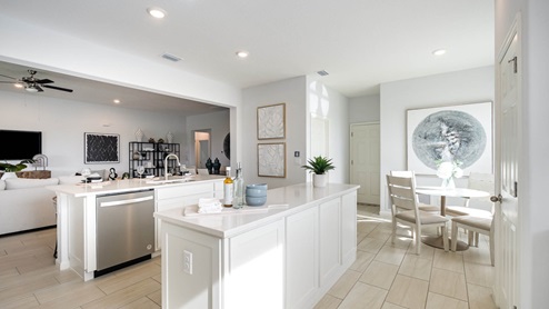 A bright, modern kitchen featuring white cabinetry, a stainless steel dishwasher, and a cozy dining area with a round table.