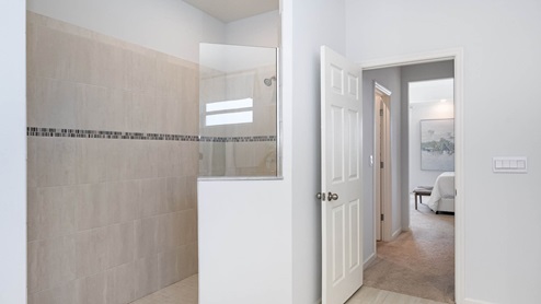 Bright, modern bathroom featuring a spacious walk-in shower with glass partition, light tile, and an open doorway leading to a cozy bedroom.