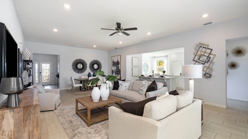 Cozy modern living room featuring light gray walls, stylish furniture, a ceiling fan, and an open view into a dining and kitchen area.