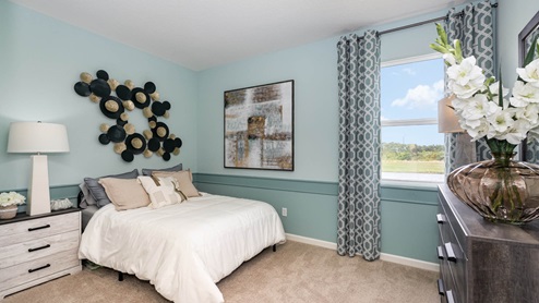 Cozy bedroom featuring a white bed, decorative wall art, modern lamp, and window with patterned curtains, all in soothing blue tones.