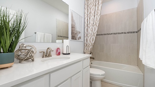 Modern bathroom featuring a white sink, decorative plants, stylish shower curtain, and neutral tile accents. Clean and inviting design.