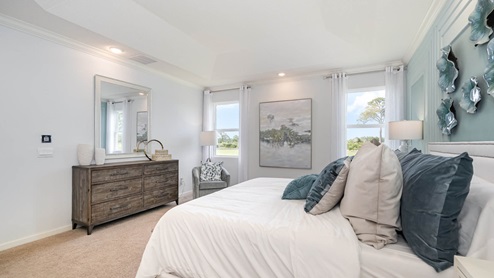 Bright, modern bedroom featuring a bed with plush pillows, a wooden dresser, art, and large windows with scenic views.