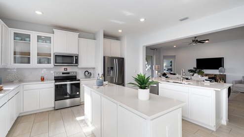 Bright, modern kitchen with white cabinetry, stainless appliances, and a large island adorned with plants and table settings.