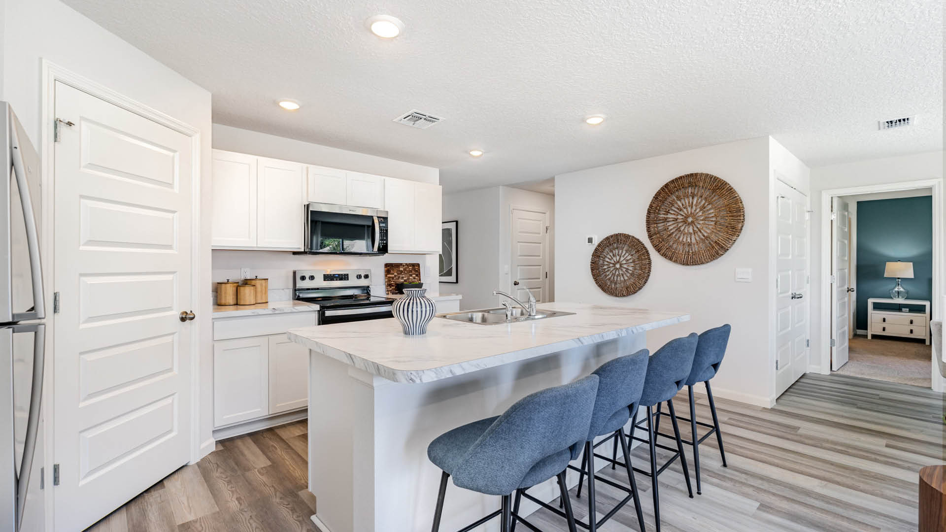 Modern kitchen with white cabinetry, stainless steel appliances, and kitchen island with blue bar stools, featuring decorative wall art.