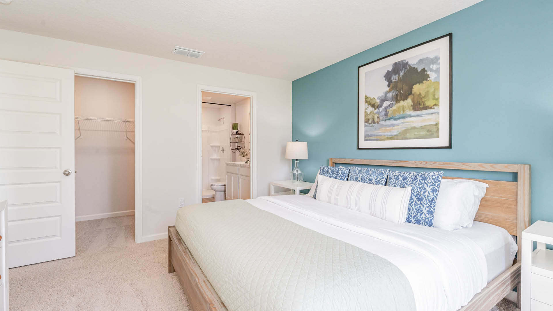 A cozy bedroom featuring a large bed with decorative pillows, a bedside lamp, and a view of an adjoining bathroom and closet.