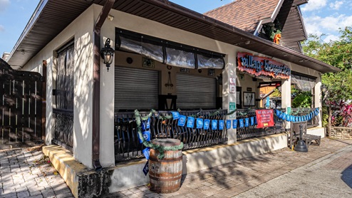 Exterior view of Village Berggarten, featuring closed shutters, blue banners, and a welcoming sign indicating the café is open.