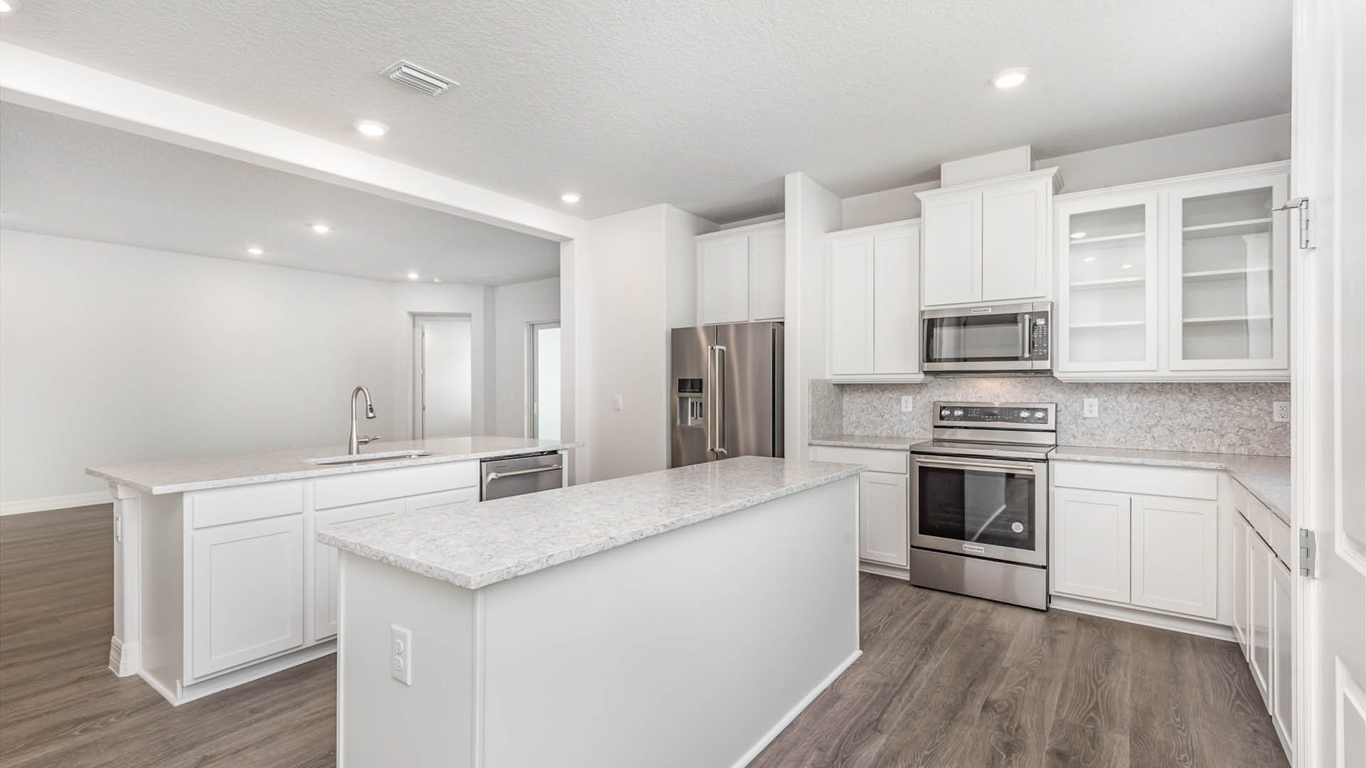 Modern kitchen with white cabinets, quartz countertops, stainless steel appliances, and an island with a sink. Bright and spacious layout.