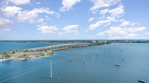 A coast view featuring a long bridge over water, and sailboats.
