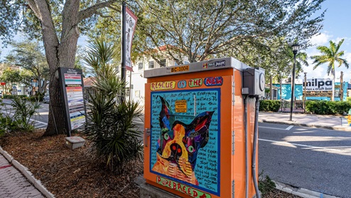 A brightly colored utility box mural featuring a dog with the text "Rescue is the new purebred" in a vibrant downtown setting.