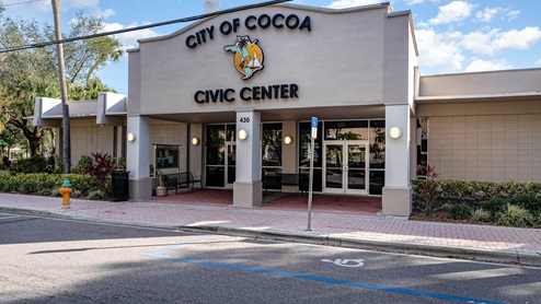 Exterior of the Cocoa Civic Center featuring modern architecture, a large sign, and landscaped surroundings, with blue sky above.