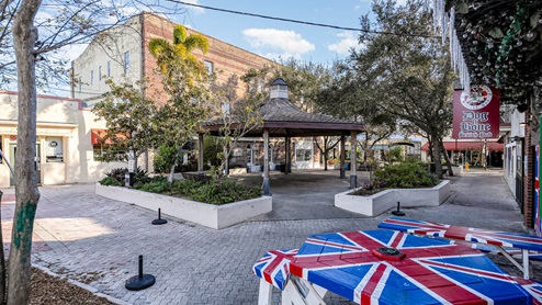 A quaint plaza featuring a gazebo, British pub sign, and colorful Union Jack table, surrounded by greenery and historic buildings.