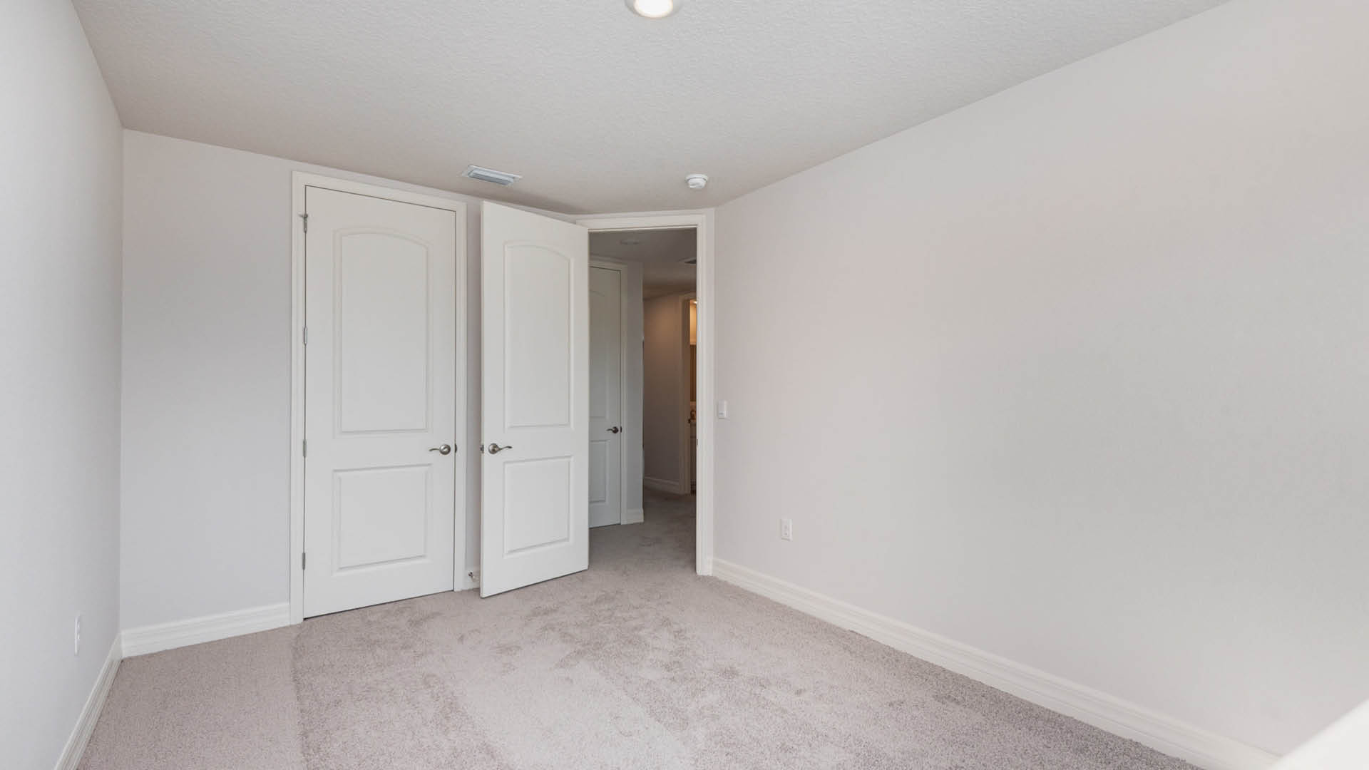Partially empty room with light gray walls, a carpeted floor, and open white double doors leading to another space.