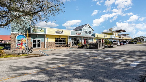 A colorful, modern shopping plaza featuring various storefronts, outdoor seating, and a mural of a playful goat.