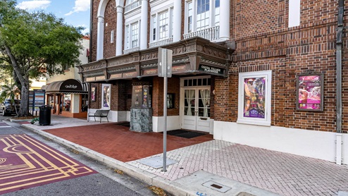 Exterior of Cocoa Village Playhouse with brick facade, marquee, and posters for shows; nearby is a cafe and street signage.