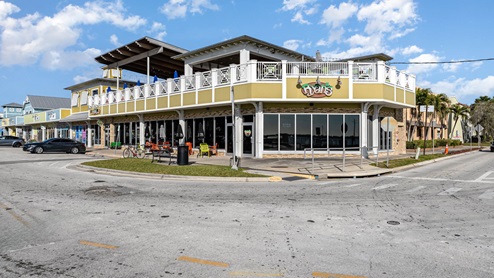 A vibrant restaurant named "Ryan's" with outdoor seating, located at a corner of a street, surrounded by colorful buildings and palm trees.