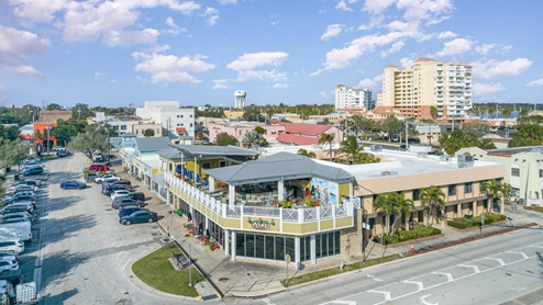 A vibrant coastal town scene featuring shops, parked cars, and colorful buildings.