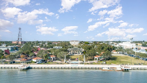 Aerial view of Cocoa, FL, featuring a waterfront park, gazebo, historic buildings, and a water tower under a partly cloudy sky.