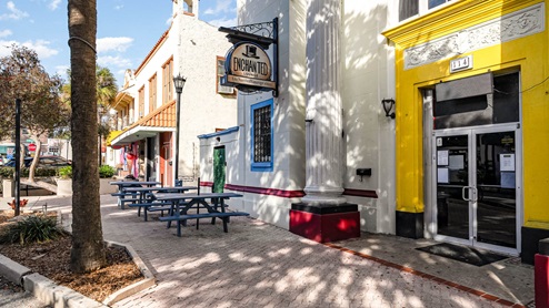 Exterior view of Enchanted Lounge with colorful walls, outdoor seating, and a welcoming atmosphere on a sunny day.