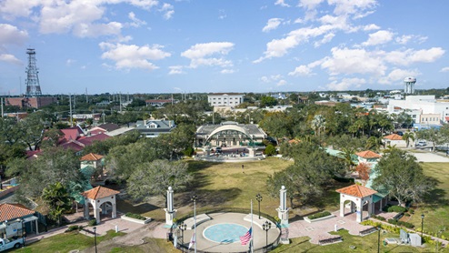 Aerial view of a vibrant park with a stage, surrounded by trees, homes, and a water tower.