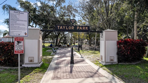 Entrance to Taylor Park, featuring a sign with park rules, surrounded by trees and vibrant landscaping.