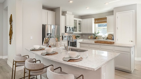 Kitchen featuring white cabinetry, stainless steel appliances, large kitchen island with sink and three white barstools.