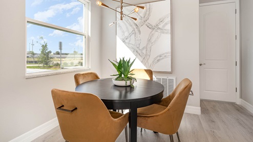 Breakfast nook with brown table and orange chairs. Large window and wall art bring a modern elegance and light to the room.