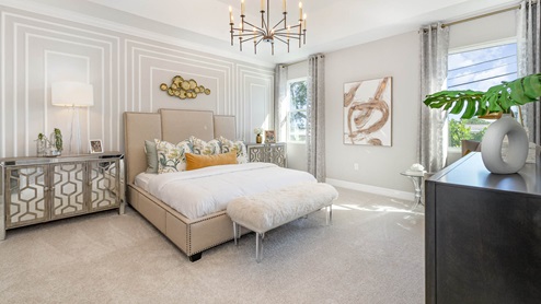 Stylish bedroom featuring a plush bed, decorative pillows, a chic chandelier, and large windows with natural light.
