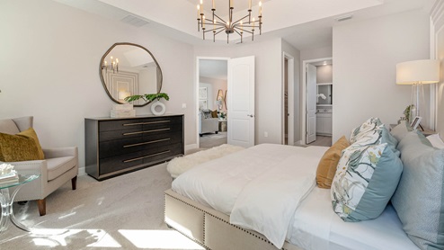 A bedroom decorated in a traditional style with large bed centered in room under large chandelier and bathroom ensuite.