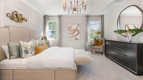 A traditional bedroom with large beige tufted bedframe, two large windows with beige and white curtains.