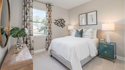A bedroom decorated in a coastal style with white furniture, featuring a bed with white and green accents, two bird prints above the headboard and window with brown and green pattern.