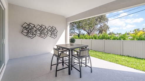 Outdoor covered lanai with a patio table and four chairs and vinyl fence for privacy.