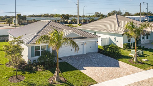 Aerial view of single-story home, metal roof, three car garage and paver driveway.