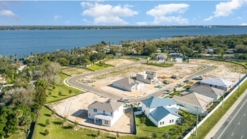 Aerial view of a new residential neighborhood by the river, featuring several homes, construction sites, and winding roads.