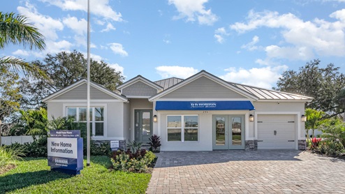 Single-story model home with a metal roof, large windows, neutral color palette and paver driveway.