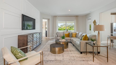 A stylish and modern living room features a neutral color palette, a large sectional sofa with yellow accent pillows, a mounted TV, and a sleek design with natural light streaming through large windows.