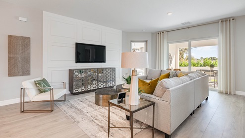 A bright living room area with beige sofas, light vinyl plank flooring and large sliding glass doors leading out to covered lanai.