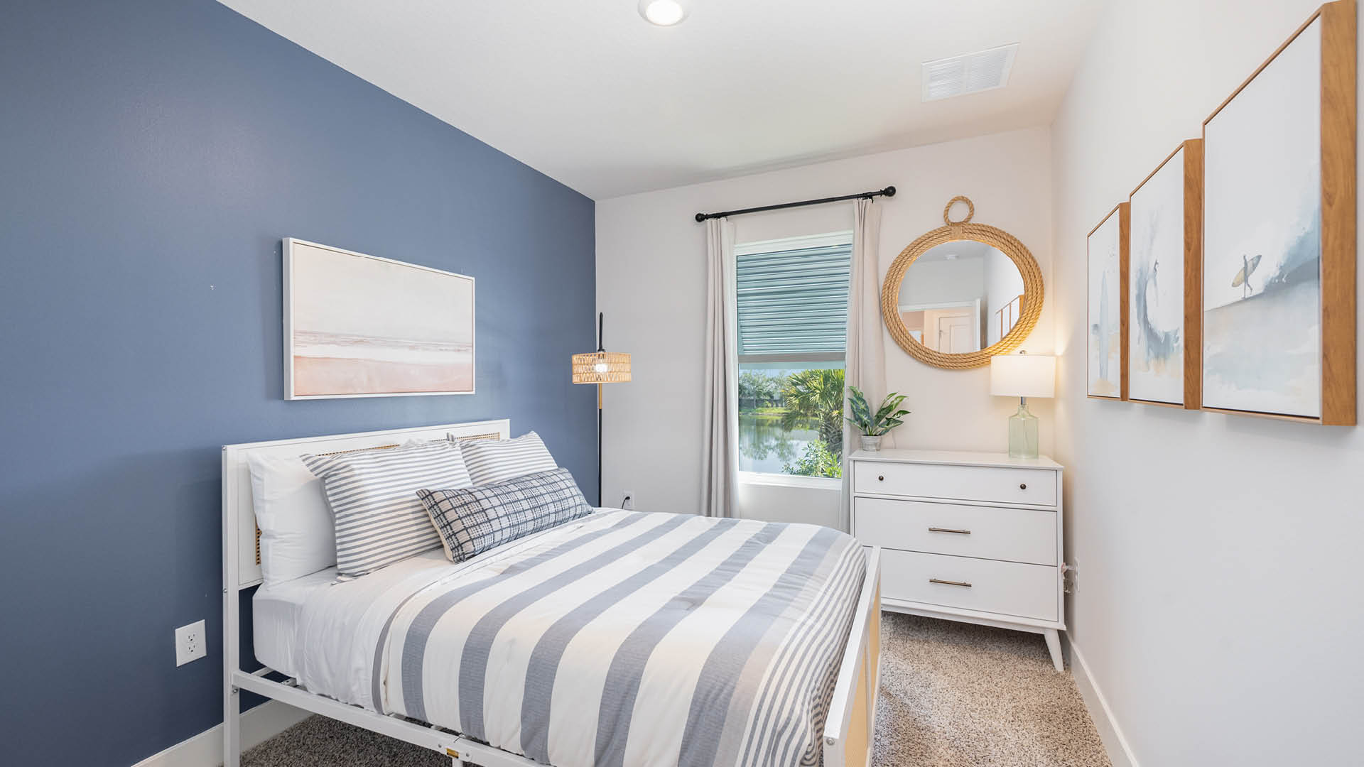 Coastal bedroom with white bed, blue accent wall and large window.