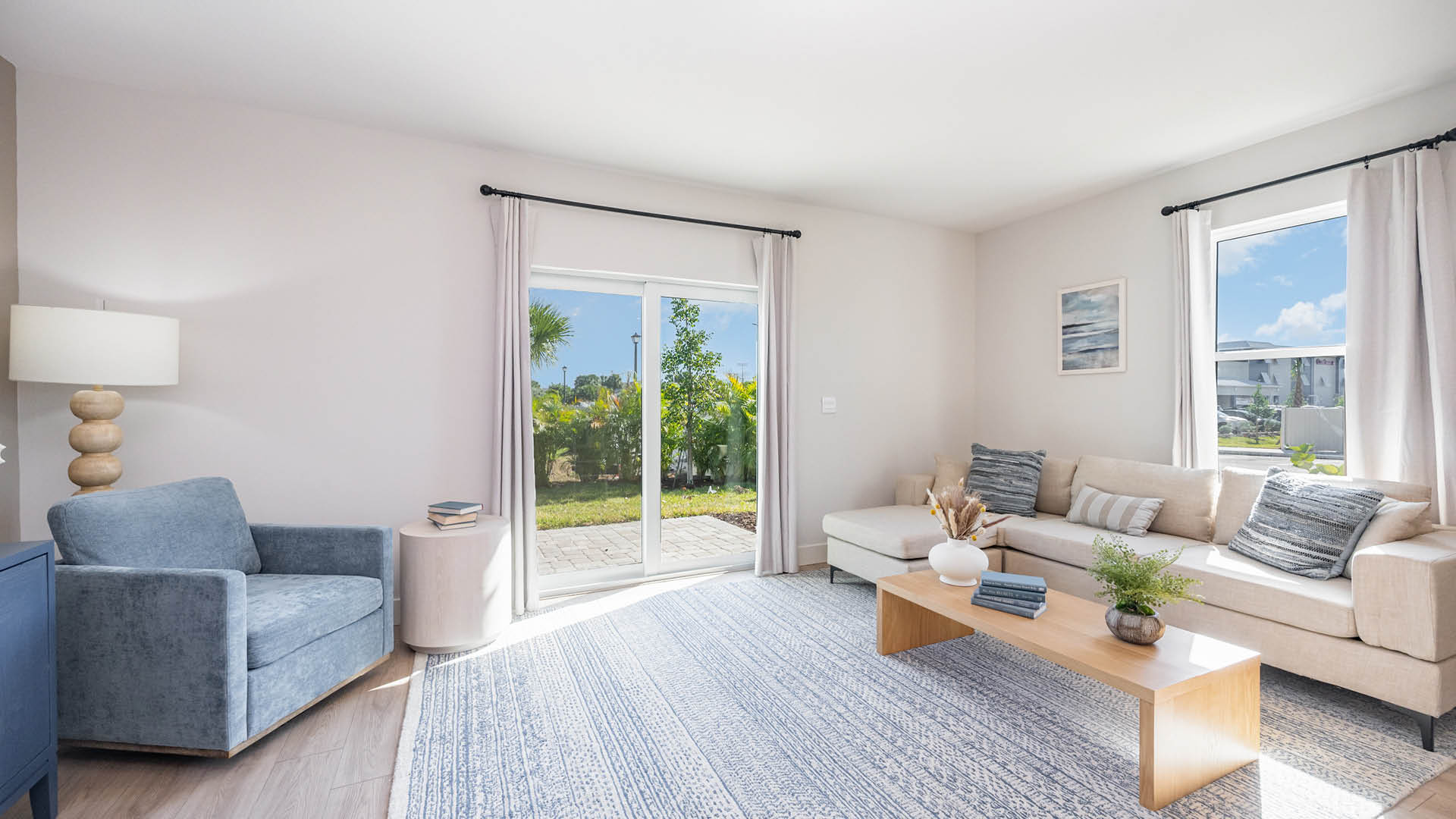 Bright living room with a light-colored sofa, blue armchair, wooden coffee table, and large sliding doors.
