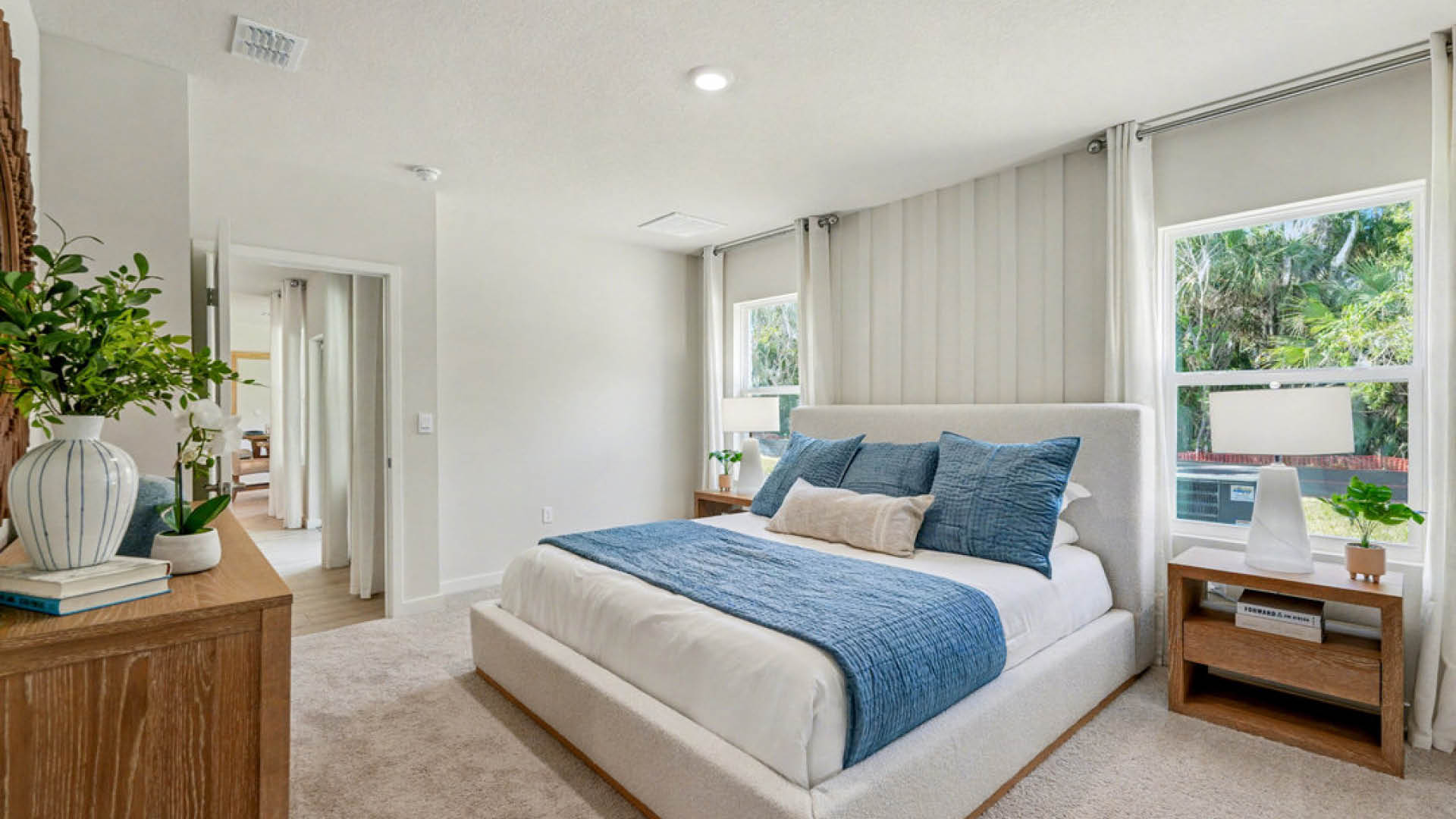 A cozy bedroom featuring a blue and white bed, complemented by soft lighting and neutral-colored walls.