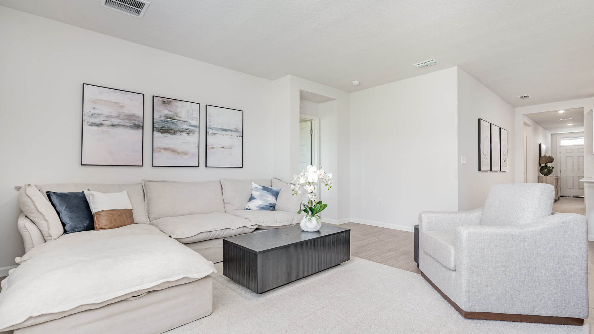 Modern living room featuring a beige sectional sofa, a dark coffee table, and abstract wall art, accented by a potted orchid.