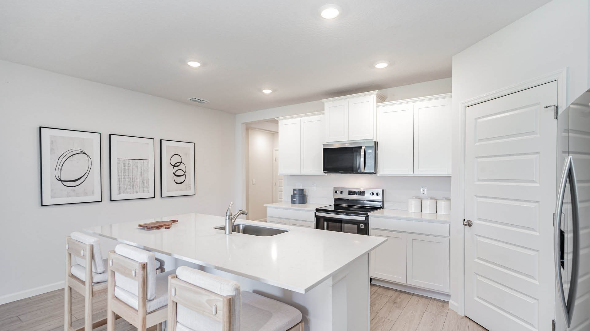Modern kitchen featuring white cabinets, stainless steel appliances, and a large island with seating. Abstract artwork adorns the walls.