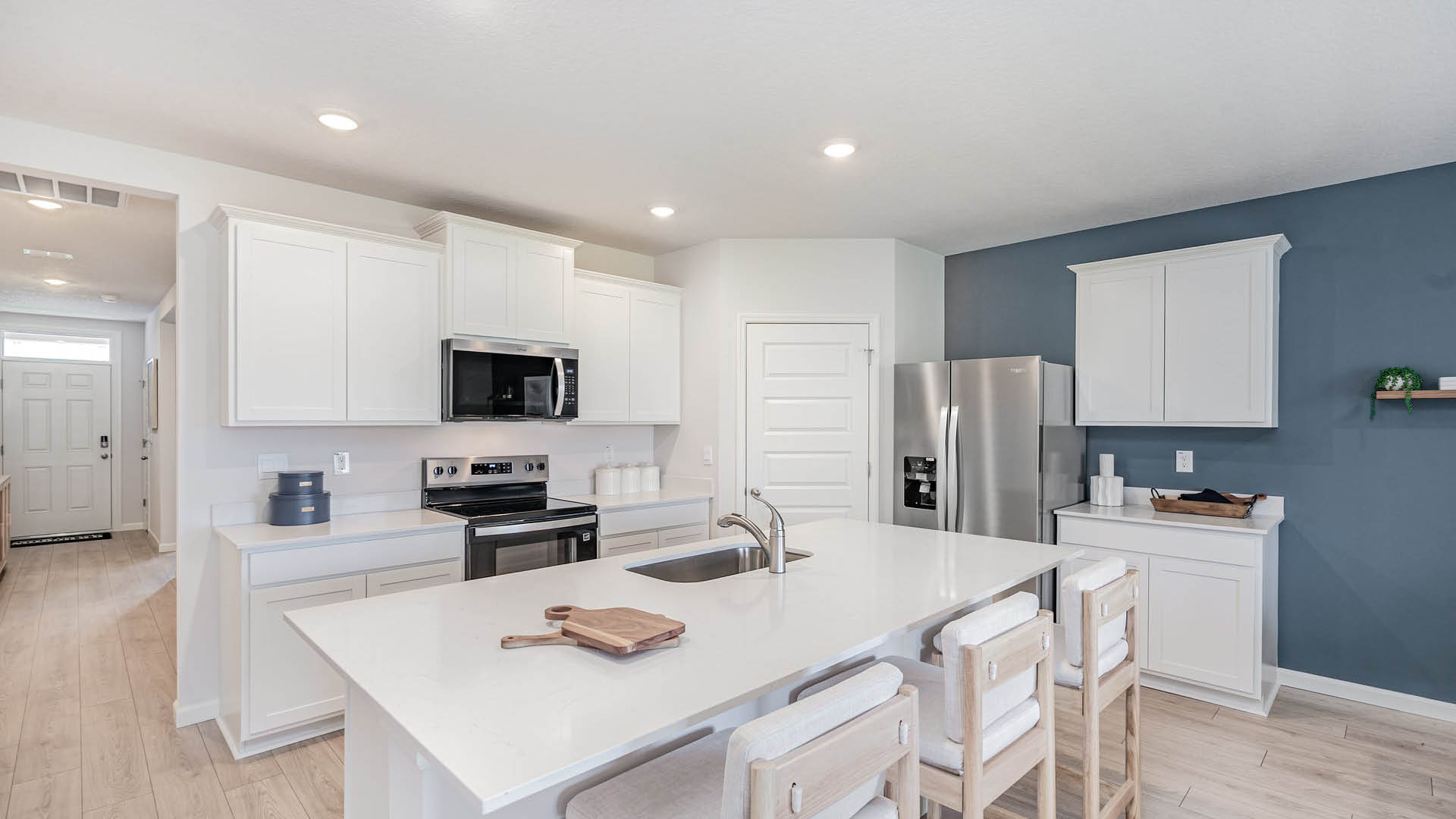 Modern kitchen with white cabinets, stainless steel appliances, a large island, and light wood flooring, featuring minimalist decor.