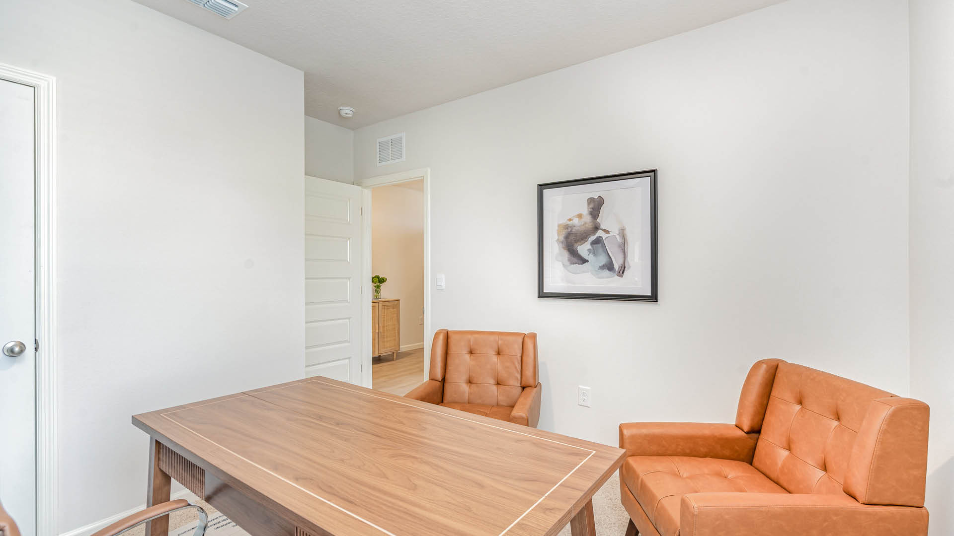 A minimalist office with two brown leather chairs, a wooden table, and an abstract painting on a white wall. Soft lighting creates a calm atmosphere.