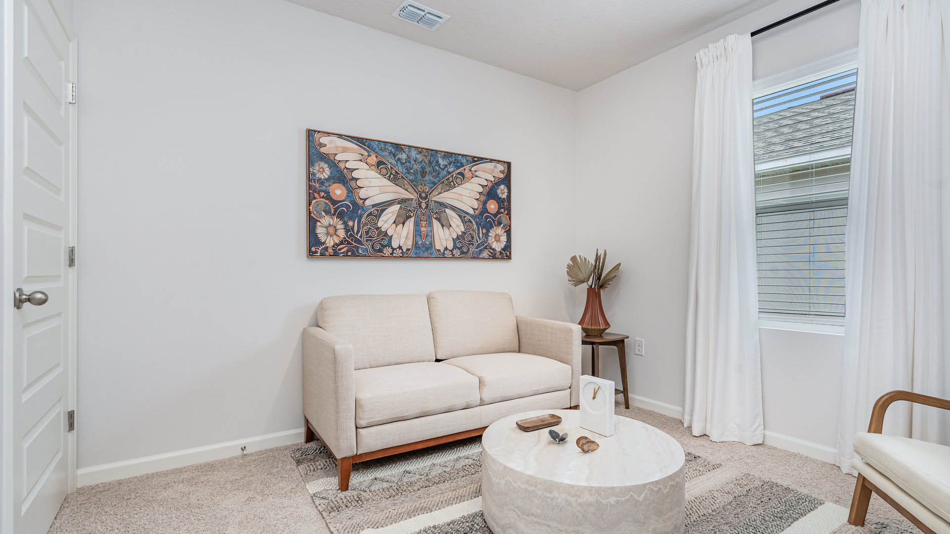 Minimalist living room with a beige sofa, butterfly artwork on the wall, round marble coffee table, and a window with sheer white curtains. Cozy and serene.