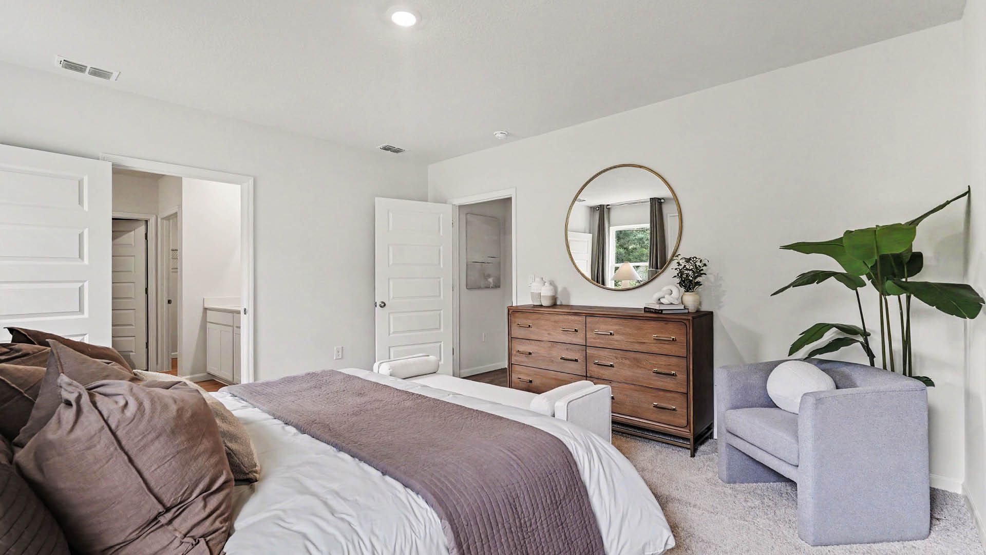 A large bedroom with beige carpet, white walls, and two windows, allowing natural light to illuminate the space. An open door leading to an ensuite bathroom is visible.