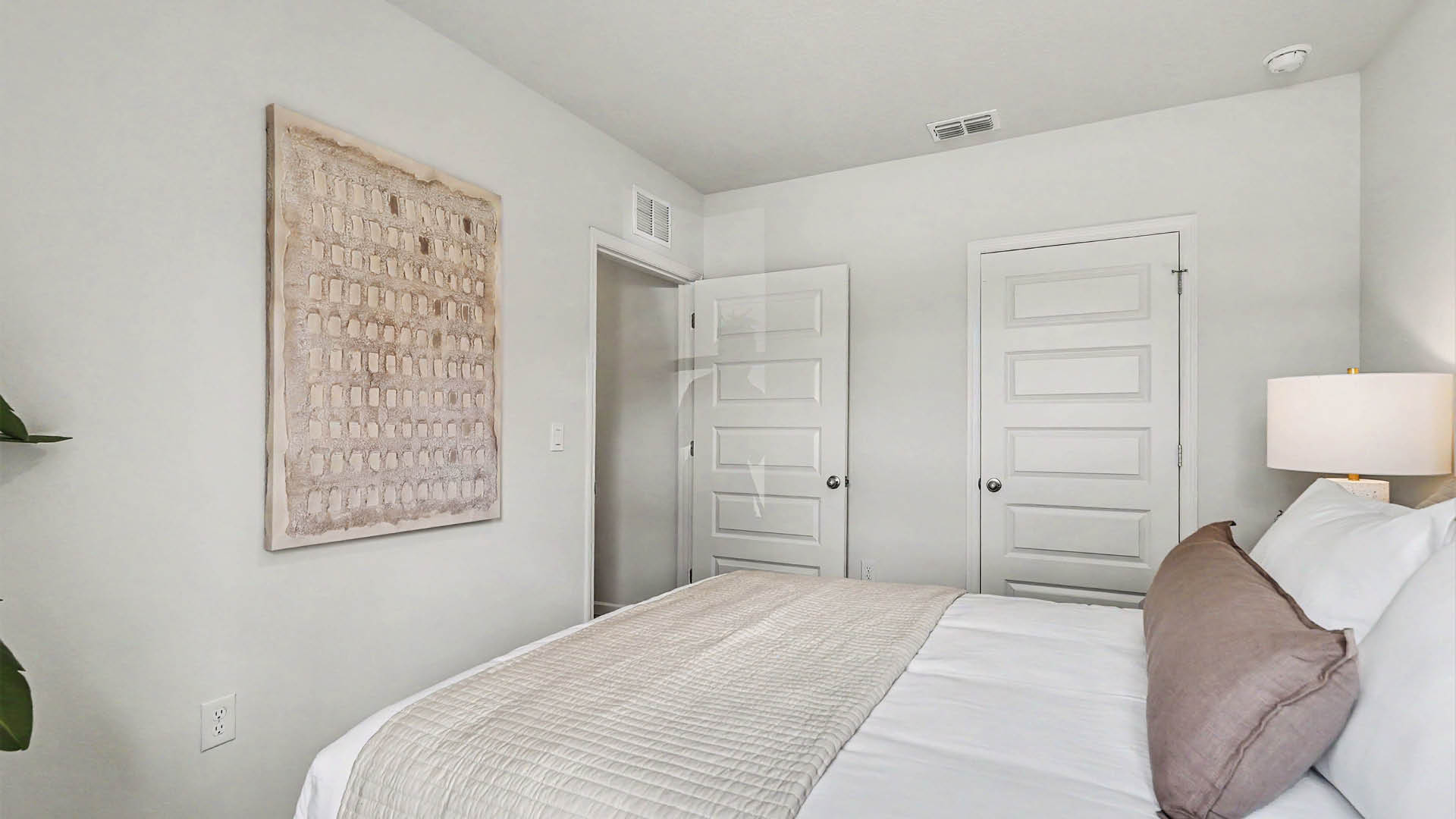 A cozy bedroom with a bed and lamp. The door to the room is open, while another door, leading to the closet, is closed.